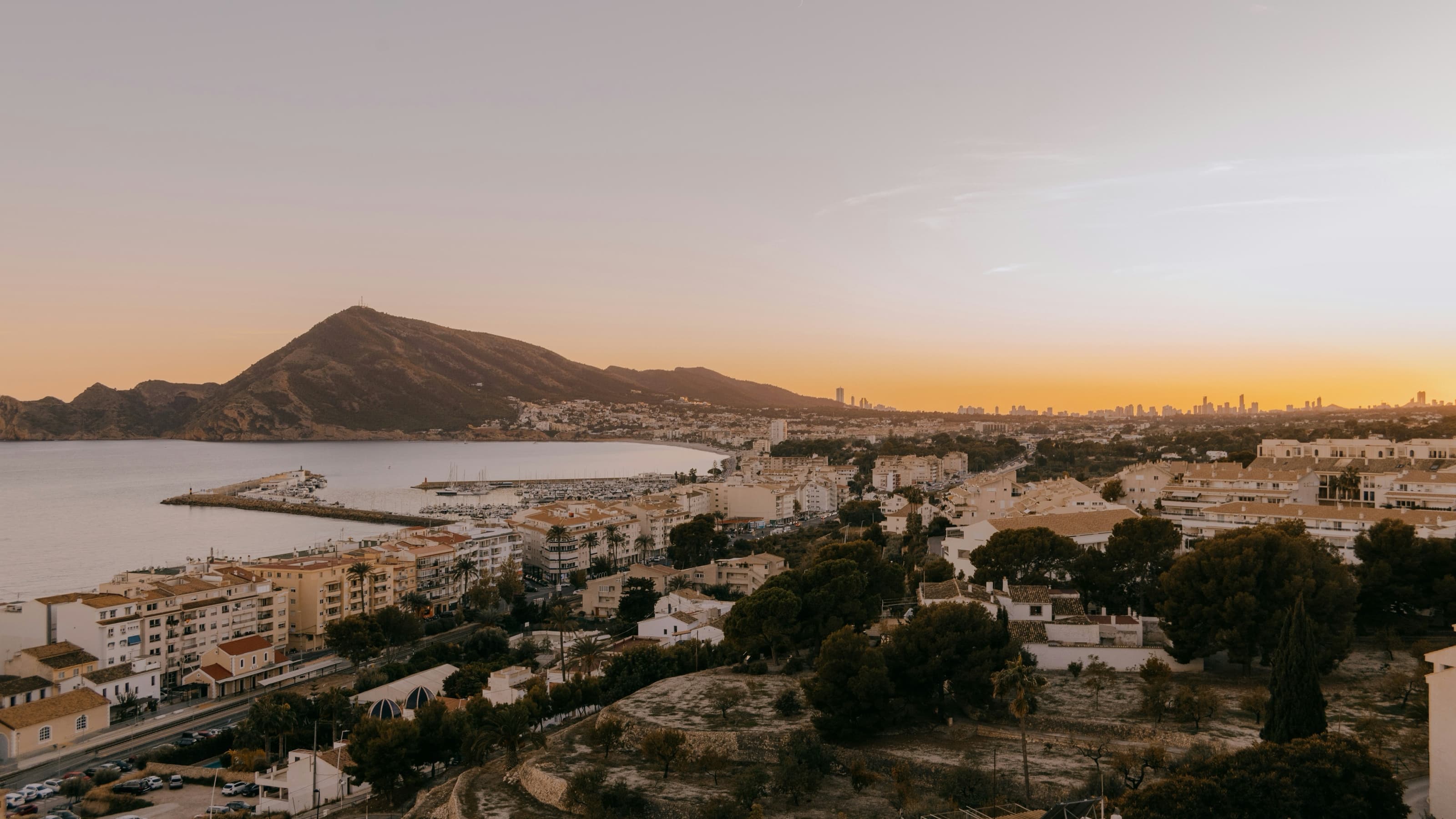 Vista aérea del casco blanco de Altea y su bahía al atardecer, con el puerto deportivo en primer término