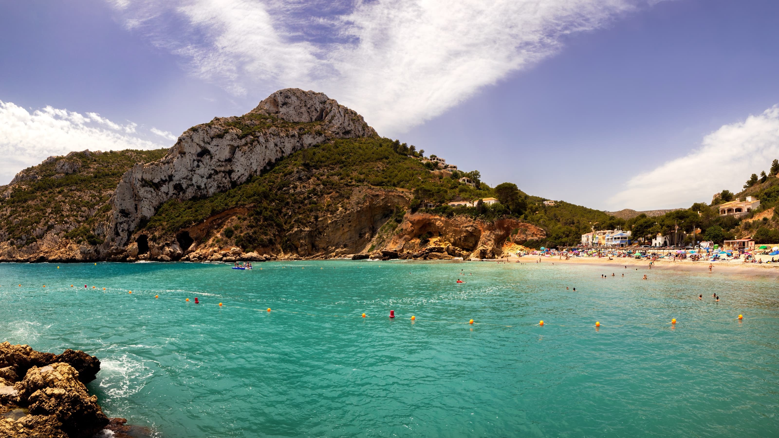Panorámica de la cala de la Granadella en verano, con agua turquesa, playa de canto y acantilados con pinada