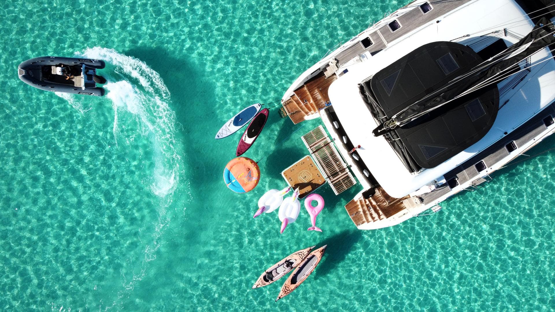 Aerial view of a Lagoon catamaran at anchor in turquoise water, surrounded by paddleboards, kayaks and water toys
